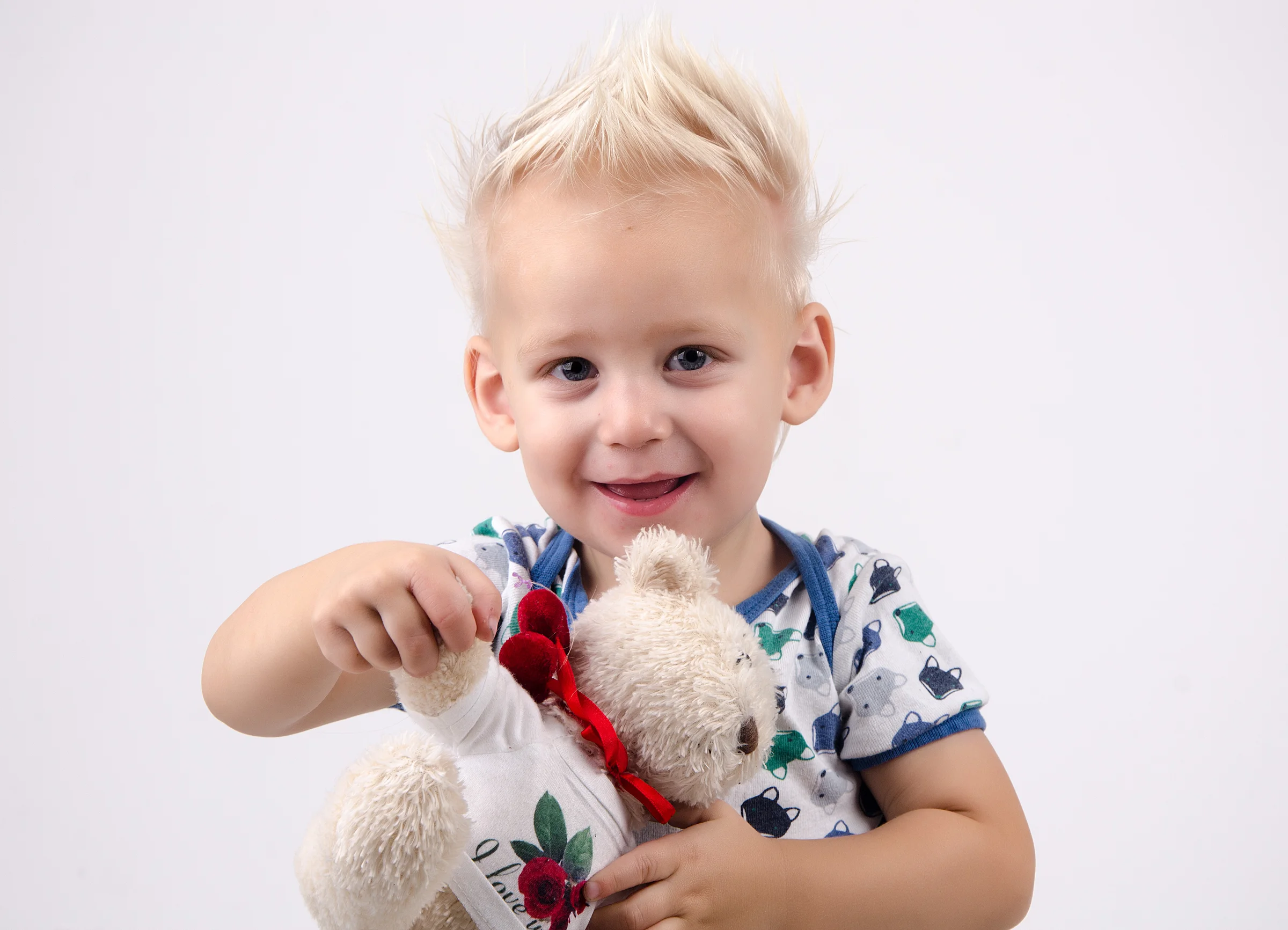 Et smilende barn med en bamse foran en lys baggrund